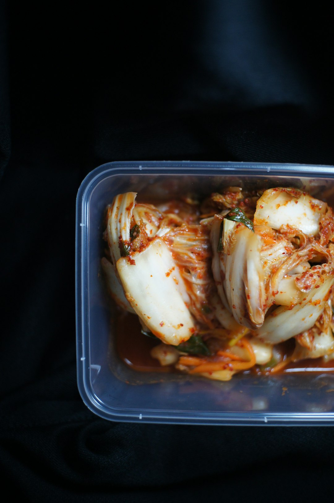 Napa cabbage kimchi in a glass jar with bright red-orange brine and visible fermented cabbage layers